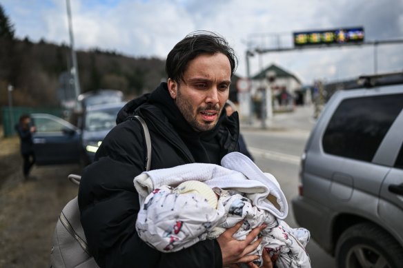 A man carries his one-month-old as he arrives in Poland after crossing the border in Kroscienko on Sunday.