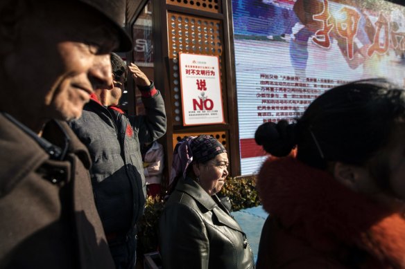 A sign warning against “uncivilised behaviour” is displayed as spectators watch a street performance in the main bazaar in Urumqi, Xinjiang. 