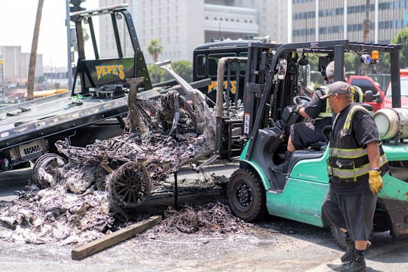 Pekerja membersihkan kendaraan Waymo yang terbakar di Los Angeles pada hari Senin.