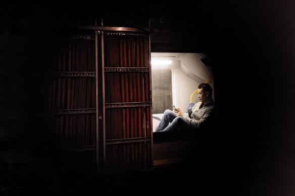 A hole in a door in an old car park that runs parallel to a platform at Sydney’s Wynyard station gives an intimate glimpse of a train passenger looking at his phone.