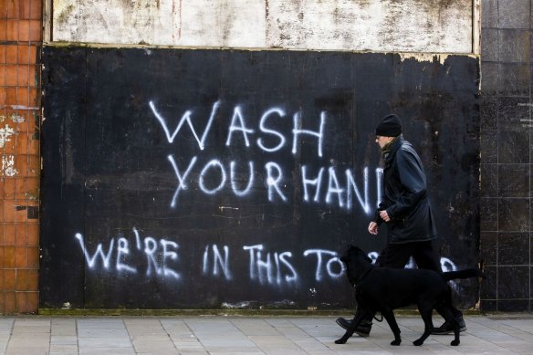 A man walks his dog past graffiti with the writing, "Wash Your Hands, We're In This Together", in Belfast, Northern Ireland, last month. 