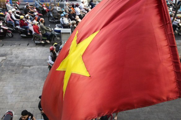 A Vietnamese national flag flies as motorcyclists wait at a traffic signal in Ho Chi Minh City, Vietnam.
