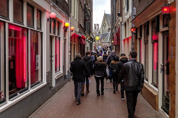 Tourists walking in the red light district of Amsterdam, where prostitutes try to lure customers from behind their windows.