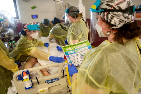 Nurses prepare to roll a patient in their bed as part of their COVID treatment process.