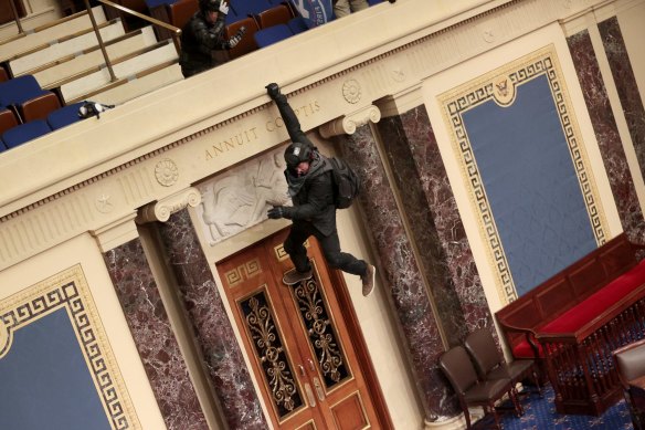 A rioter hangs from the balcony in the Senate chamber.
