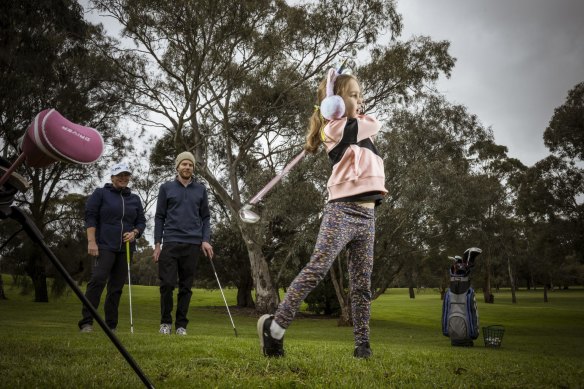 Matilda Gray is watched by her  father Lincoln and PGA  Community Instructor Claire Trail at the Northcote Public Golf Course. 