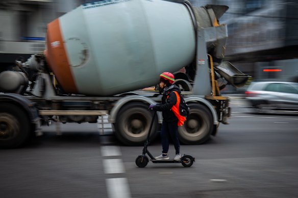 An e-scooter rider alongside a concrete mixer.