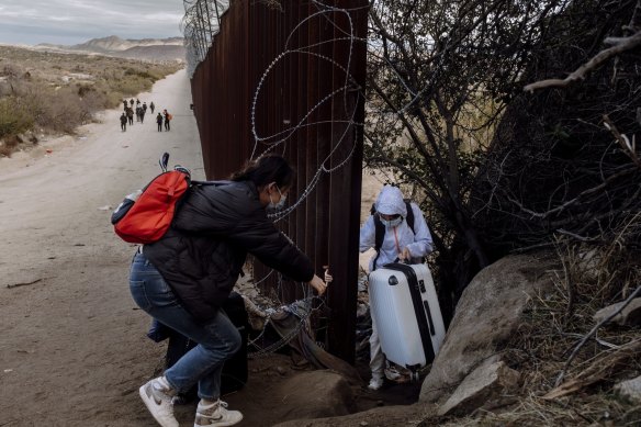 Migrants cross through a gap in the US-Mexico border fence in Jacumba Hot Springs, California.
