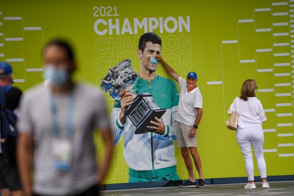 A spectator places a mask over the face of Novak Djokovic on a billboard at Melbourne Park.