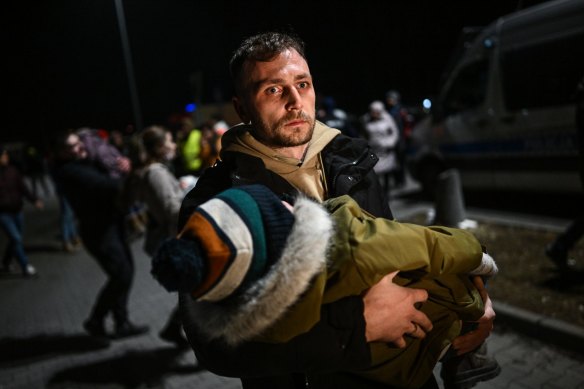 A man holds a sleeping baby after arriving by bus to a supermarket parking lot from the Polish-Ukrainian border crossing in Przemysl, Poland. 