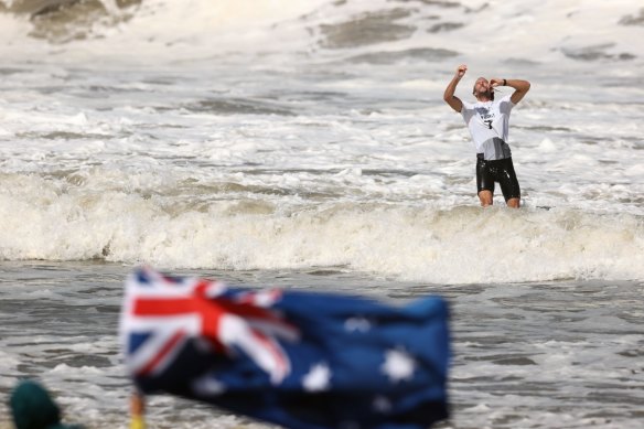 Owen Wright takes a moment in the surf to let his bronze medal sink in as an Australian flag flutters in the foreground.