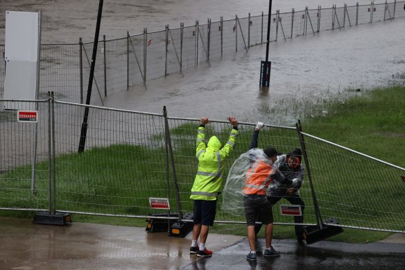 Men struggle to lift a fallen fence that surrounds the Powerhouse Museum site, impacted by the Parramatta River. 