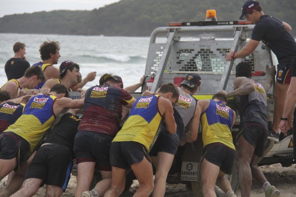 Brisbane Lions players push a truck out of sand on their pre-season camp in 2014.