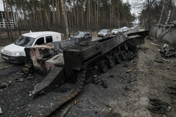 Cars drive past a destroyed Russian tank as a convoy of vehicles evacuating civilians leaves Irpin, on the outskirts of Kyiv.