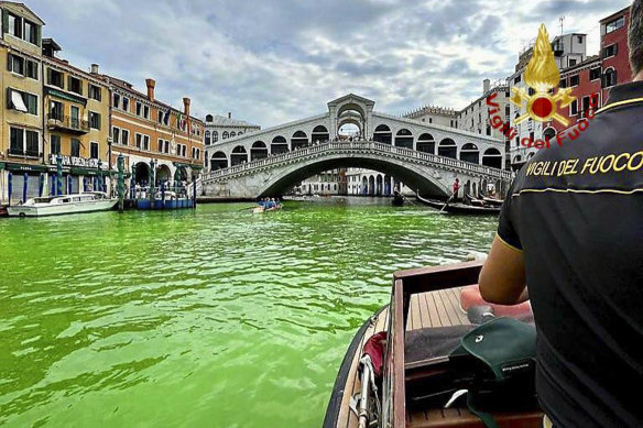 A firefighter on a boat looks at the arched Rialto Bridge along Venice’s historical Grand Canal as a patch of phosphorescent green liquid spreads.