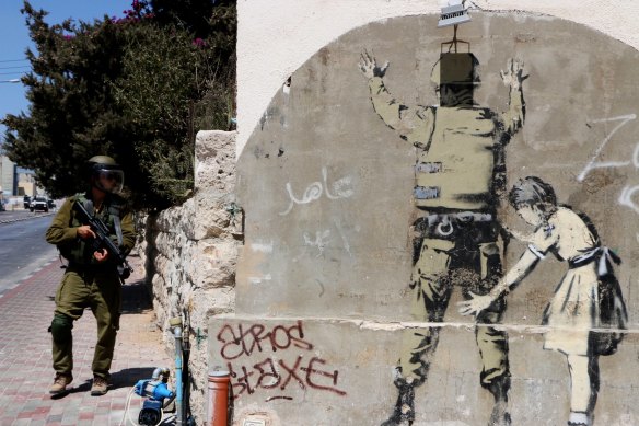An Israeli soldier walks past Banksy graffiti in Bethlehem, West Bank.