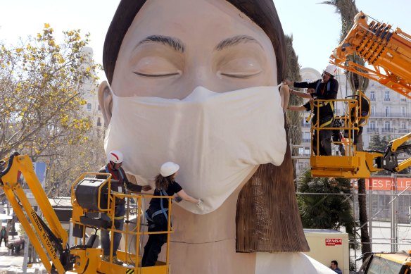 Workers place a mask on the figure of the Fallas festival in Valencia.
