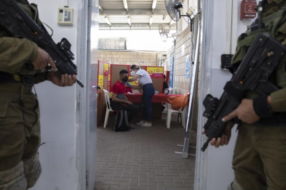 Israeli soldiers stand guard as a Palestinian who works in Israel receives a Moderna COVID-19 vaccine at the Tarqumiya crossing between the West Bank and Israel.