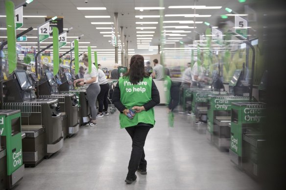 An employee supervises self-service checkout kiosks at a Woolworths store.