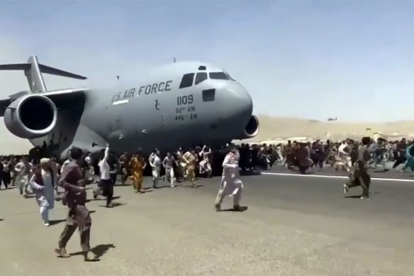 People run alongside a US Air Force transport plane as it moves down a runway of the international airport in Kabul.