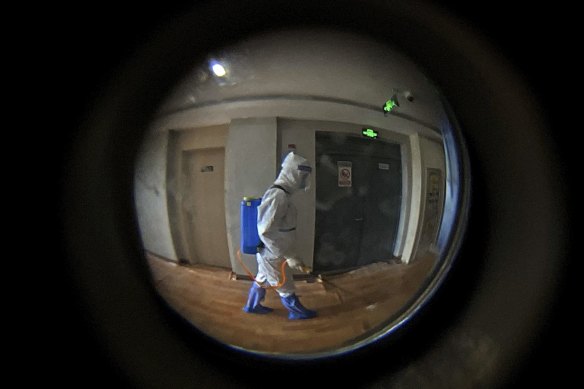 Seen through a door peephole, a medical worker wearing a protective clothing disinfects the corridor of a hotel used for foreigners to stay during a period of health quarantine in Shanghai in August. 