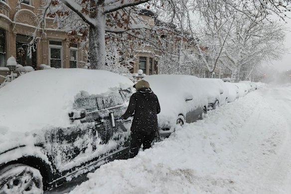 A driver clears snow off a vehicle in Brookyln.