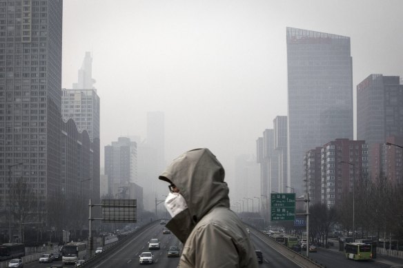 A man wearing a face mask walks on a footbridge as buildings shrouded in haze stands in the background in Beijing, China.