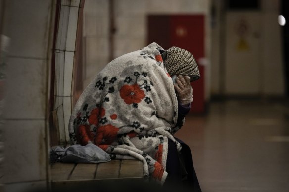 An elderly woman sits on a bench wrapped in a blanket in a subway station turned into a shelter in Kyiv, Ukraine.