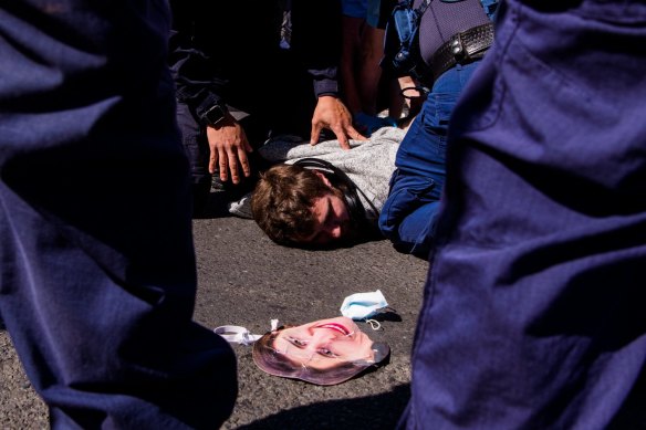 A protester is detained by police as a Gladys Berejiklian mask rests on the ground.
