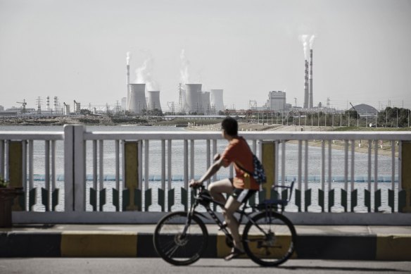 A man rides a bicycle over a bridge as power plants stand in the distance in Baotou, Inner Mongolia. 