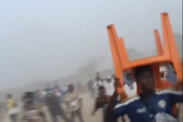 In this grab taken from video provided by Nimba Sports Zaly, a man holds a chair on top of his head in a stampede, during a soccer match at the Stade de Nzérékoré, Guinea.