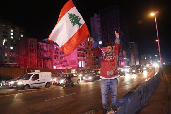 An anti-government protester flashes the victory sign and waves a Lebanese flag in Beirut, Lebanon.