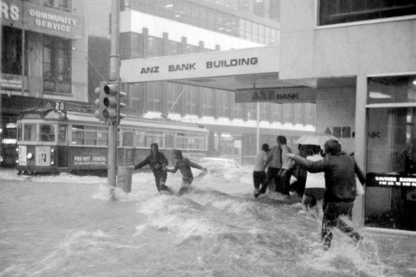Home-bound workers brave the surging flood waters at the corner of Flinders Lane and Elizabeth Street. 