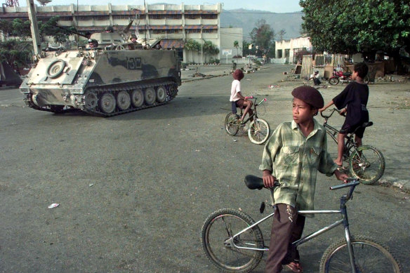 East Timorese boys ride their bicycles as an Australian armoured personnel carrier rolls down the street during a security sweep in Dili, September 1999.