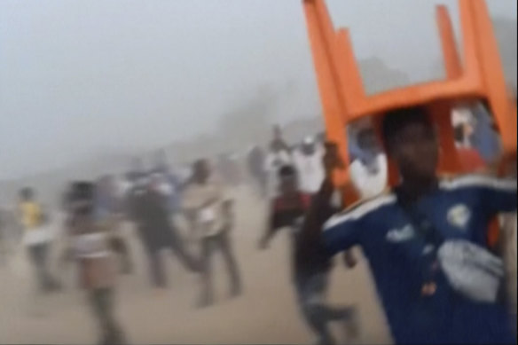 In this grab taken from video provided by Nimba Sports Zaly, a man holds a chair on top of his head in a stampede, during a soccer match at the Stade de Nzérékoré, Guinea.