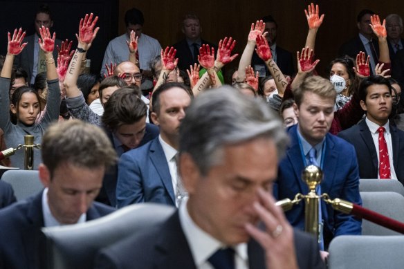 Protesters raise their hands while demonstrating behind US Secretary of State Antony Blinken.