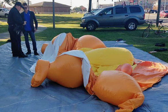 A responding officer and an unidentified man stands by the deflated Baby Trump balloon that was knife in Tuscaloosa, Alabama. 