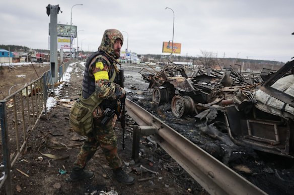 An armed man stands by the remains of a Russian military vehicle in Bucha, close to the capital Kyiv