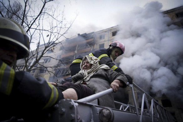 Ukrainian firefighters evacuate an elderly woman from an apartment building hit by shelling in Kyiv. 