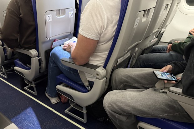 Passengers seated inside an airplane cabin with visible seat belts, legroom, and personal belongings during a commercial flight