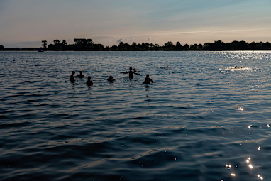 A group of people swim and wade in a calm lake during sunset - Netherlands