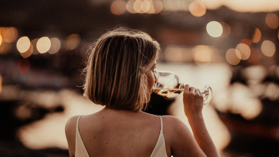 a lady in evening gown with a glass of white wine enjoying sunset sitting at a river Douro bank.