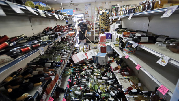 Bottles of wine are strewn in the middle of an aisle as Victor Abdullatif mops inside of his family's store in Ridgecrest. 