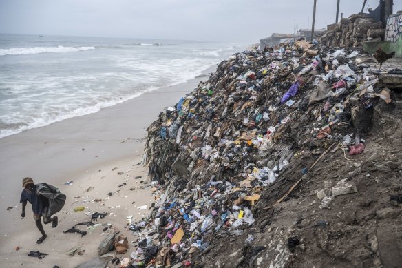 A trash picker walks by piles of  textile waste on the shoreline at Chorkor beach in Accra, Ghana.  