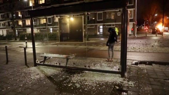 A person stands at a bus stop where the glass has been shattered after rioting, in Haarlem, Netherlands. 