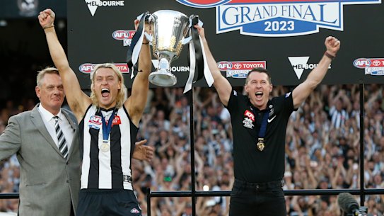 Former Collingwood captain Peter Moore presents the premiership cup to his son and current Collingwood captain Darcy Moore and coach Craig McRae.