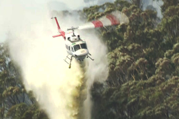 A helicopter douses an out-of-control fire near Rawson with water on Sunday.