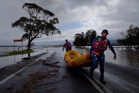 An SES crew carries their boat from the floodwaters that have partially submerged Bolong Road at Shoalhaven Heads.