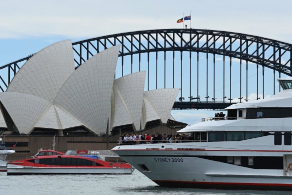 People stand on the deck of a Captain Cook Cruise vessel near the Opera House and the Sydney Harbour Bridge, while flags fly at half-mast for Queen Elizabeth II.