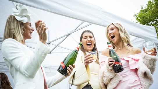 Caroline Knipe, Jasmine Ryan-Watson and Chelsea Matters crack open a champagne in the rain at the Melbourne Cup.